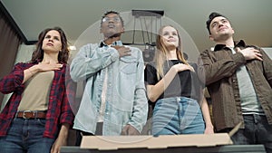 Multi ethnic group of friends listening and singing national anthem standing and hand on heart before football match in pub