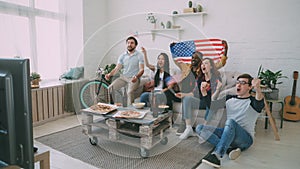 Multi ethnic group of friends with USA national flags watching sport championship on TV together cheering up their