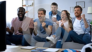 Multi-ethnic group of friends watching football game at home, celebrating goal