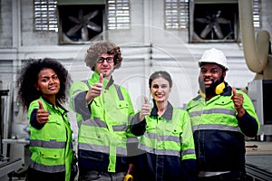 Multi-ethnic group of industrial women men worker team wearing helmet and safety vest, standing giving thumbs up at CNC