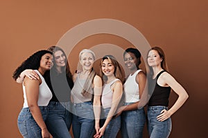 Multi-ethnic group of women of different ages posing against brown background looking at camera