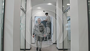 Multi ethnic installers in uniform sets up security cameras in office corridor