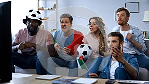 Multi-ethnic Italian fans sitting on sofa and watching game, supporting team