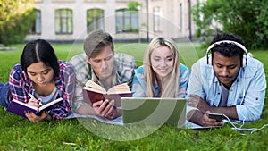 Multi-ethnic men and women doing homework on grass on campus, higher education