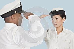 Multi-ethnic US Navy officers saluting each other over light blue background