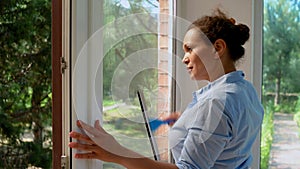 Multi-ethnic woman, maid, housewife, homemaker spraying detergent and cleaning windows in the veranda. Household Chores