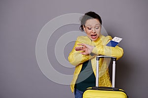 Multi-ethnic woman in yellow jacket, checks time on her wrist watch, feeling anxious being unpunctual at her flight