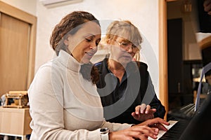 Multi ethnic young adult woman learning playing the pianoforte with her teacher indoor
