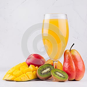Multi fruit tropical juice in elegant glass with different fruits on white wood board, square.