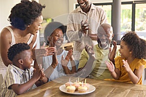 Multi-Generation Family Celebrate Grandmother's Birthday With Cake And Candles Around Table At Home 