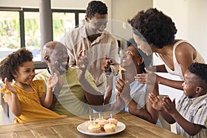 Multi-Generation Family Celebrate Grandmother's Birthday With Cake And Candles Around Table At Home 