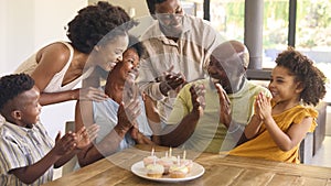 Multi-Generation Family Celebrate Grandmother's Birthday With Cake And Candles Around Table At Home 