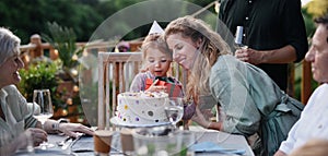 Multi generation family celebrating birthday of little girl and having garden party outside on patio.