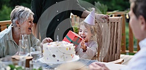 Multi generation family celebrating birthday of little girl and having garden party outside on patio.