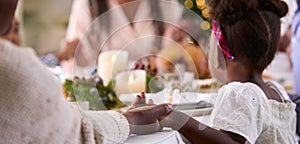 Multi-Generation Family Celebrating Christmas At Home Saying Prayer Before Eating Meal Together