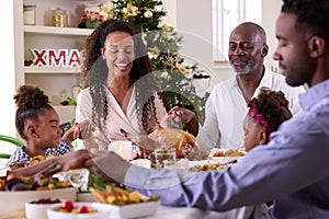 Multi-Generation Family Celebrating Christmas At Home Saying Prayer Before Eating Meal Together