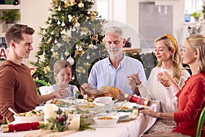 Multi-Generation Family Celebrating Christmas At Home Saying Prayer Before Eating Meal Together