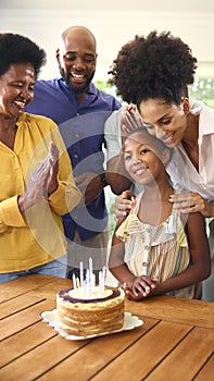 Multi-Generation Family Celebrating Granddaughter's Birthday With Cake And Candles At Home