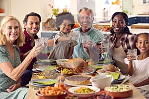 Multi-Generation Family Celebrating Thanksgiving At Home Eating Meal And Doing Cheers With Water