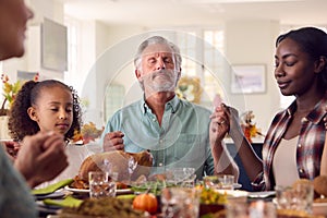 Multi-Generation Family Celebrating Thanksgiving At Home Saying Prayer Before Eating Meal Together