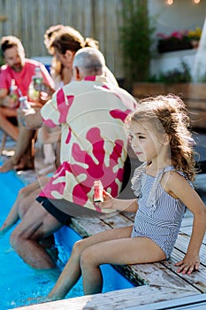 Multi generation family enjoying summer time, sitting at backyard pool.