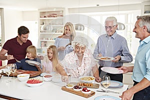 Multi-Generation Family And Friends Eating Food In Kitchen At Celebration Party