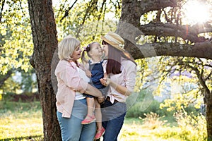 Multi generation family in the garden in summer. Retired grandmother holds beautiful little girl on hands, while she is