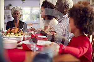 Multi Generation Family Hold Hands Around Table At Home Saying Grace Before Eating Christmas Meal