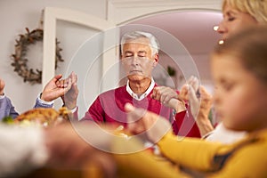 Multi Generation Family Hold Hands Around Table At Home Saying Grace Before Eating Christmas Meal