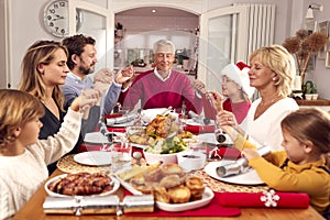 Multi Generation Family Hold Hands Around Table At Home Saying Grace Before Eating Christmas Meal