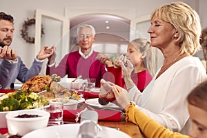 Multi Generation Family Hold Hands Around Table At Home Saying Grace Before Eating Christmas Meal