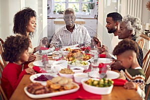 Multi Generation Family Hold Hands Around Table At Home Saying Grace Before Eating Christmas Meal