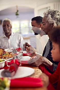 Multi Generation Family Hold Hands Around Table At Home Saying Grace Before Eating Christmas Meal