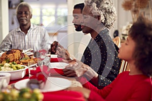 Multi Generation Family Hold Hands Around Table At Home Saying Grace Before Eating Christmas Meal