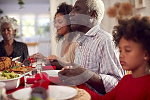 Multi Generation Family Hold Hands Around Table At Home Saying Grace Before Eating Christmas Meal