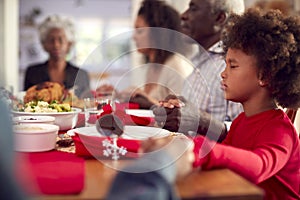 Multi Generation Family Hold Hands Around Table At Home Saying Grace Before Eating Christmas Meal