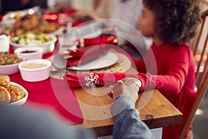 Multi Generation Family Hold Hands Around Table At Home Saying Grace Before Eating Christmas Meal