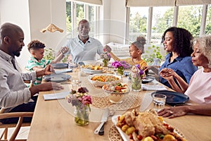 Multi Generation Family Holding Hands Around Table At Home Saying Grace Before Eating Meal Together