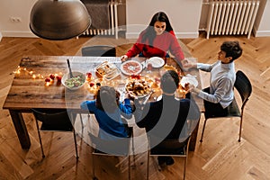 Multi generation family holding hands and praying before christmas meal while sitting at dinner table