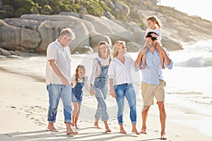 Multi generation family holding hands and walking along the beach together. Caucasian family with two children, two