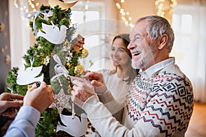 Multi-generation family indoors at home at Christmas, decorating tree.