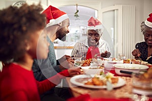 Multi Generation Family In Paper Hats Enjoying Eating Christmas Meal At Home Together