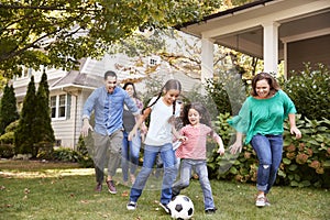 Multi Generation Family Playing Soccer In Garden