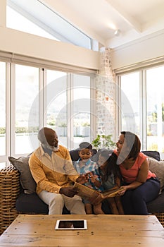 Multi-generation family reading a story book in living room