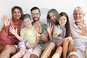 Multi Generation Family Sitting Against Wall And Waving