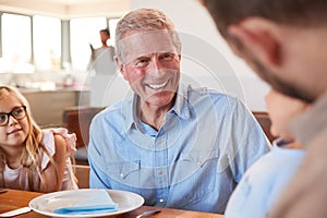 Multi-Generation Family Sitting Around Table Enjoying Meal At Home Together