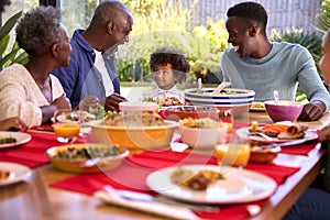 Multi-Generation Family Sitting Around Table At Home Enjoying Meal Together