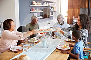 Multi-Generation Family Sitting Around Table At Home Enjoying Meal Together