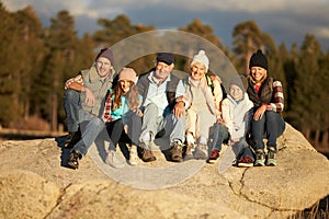 Multi generation family sitting on rocky outcrop near a forest