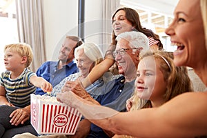 Multi-Generation Family Sitting On Sofa At Home Eating Popcorn And Watching Movie Together